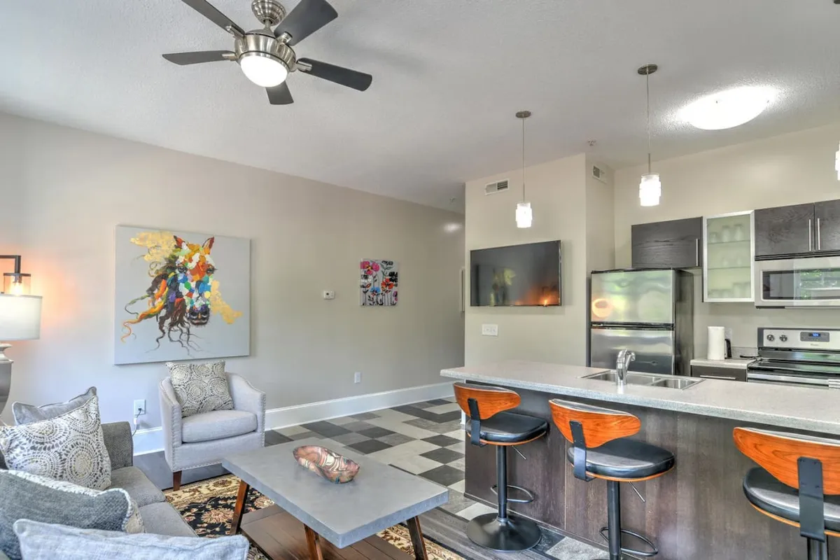 A cozy interior scene with a comfortable seating area, vibrant artwork on the wall, and a view toward the kitchen island. The setting encourages relaxation and conversation, with inviting textures and thoughtful design touches.