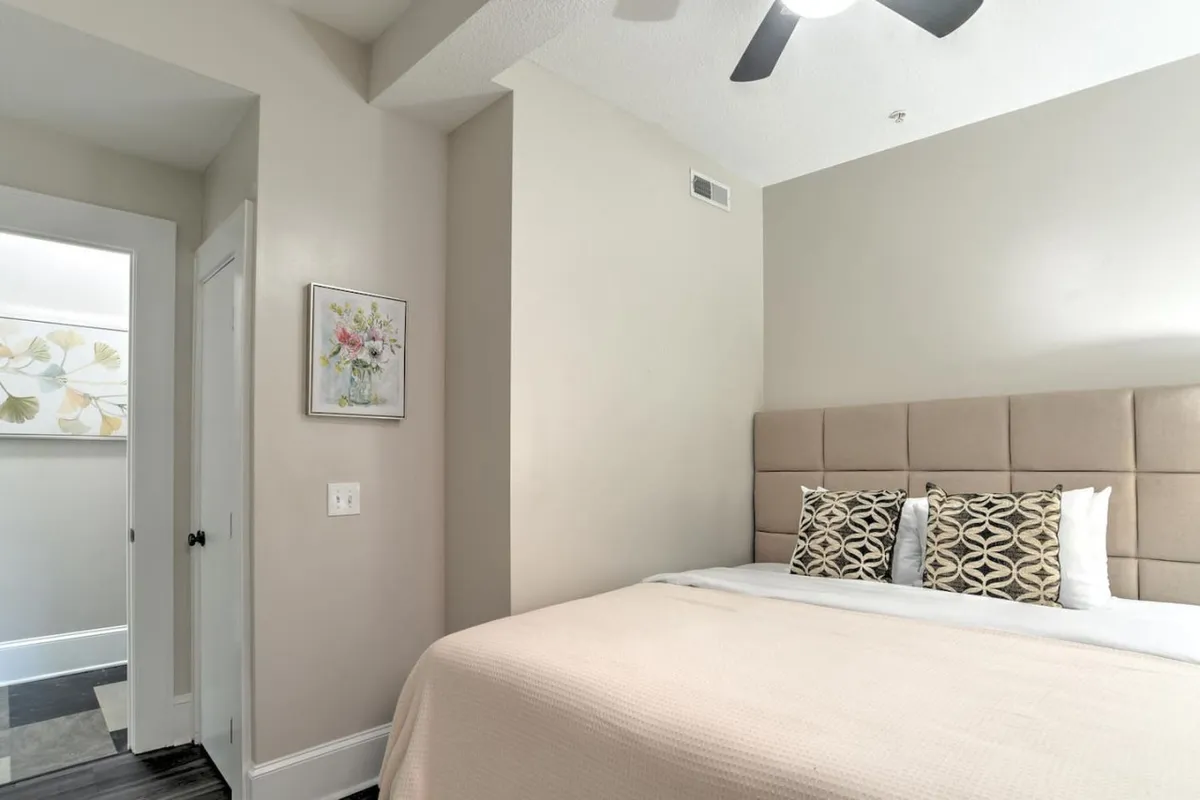 A tranquil upper-level bedroom scene with a bed dressed in plush pillows, framed floral artwork above the headboard, and a ceiling fan. The space exudes quiet warmth and encourages relaxation and reflection, offering a sense of privacy and calm.